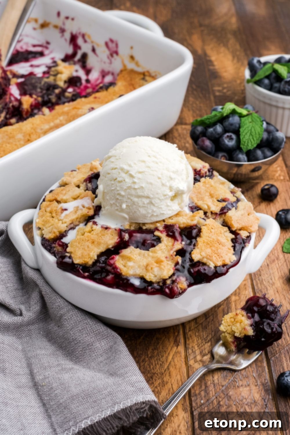 Blueberry Dump Cake in a bowl with a rectangle dish full of dump cake to the side with a bowl of blueberries