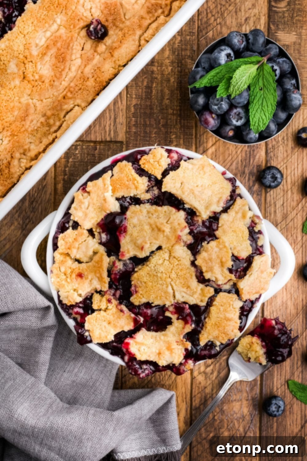 a bowl full of Blueberry Dump Cake with more cake to the side of cake in a pan