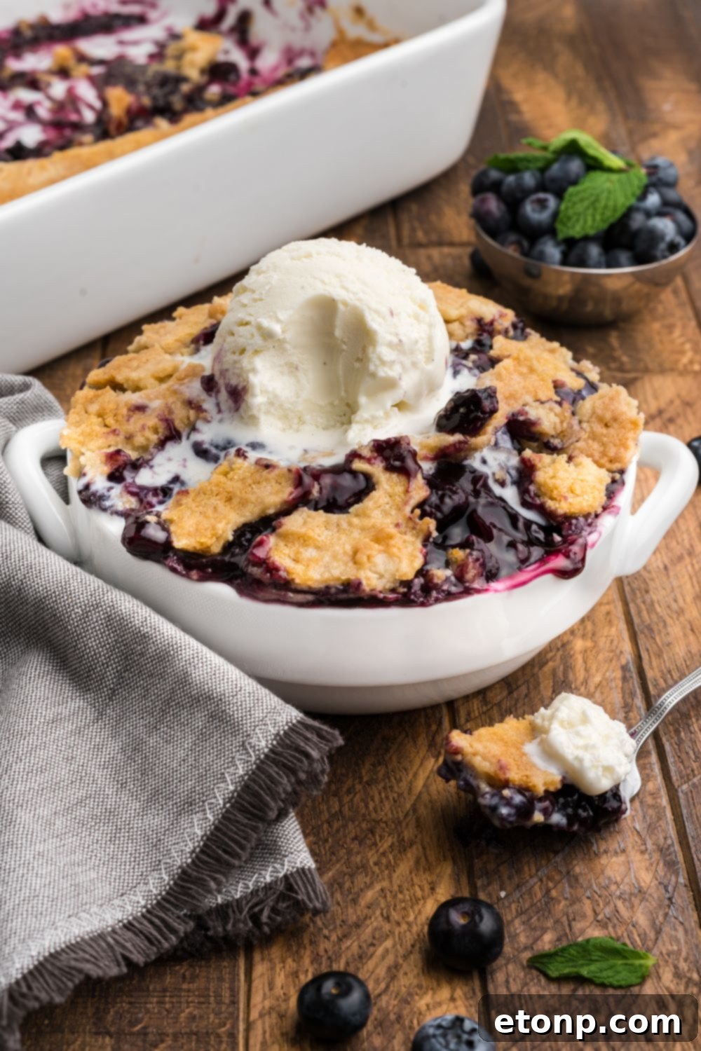 Blueberry Dump Cake in a white bowl, with ice cream in center with a bite taken out of it