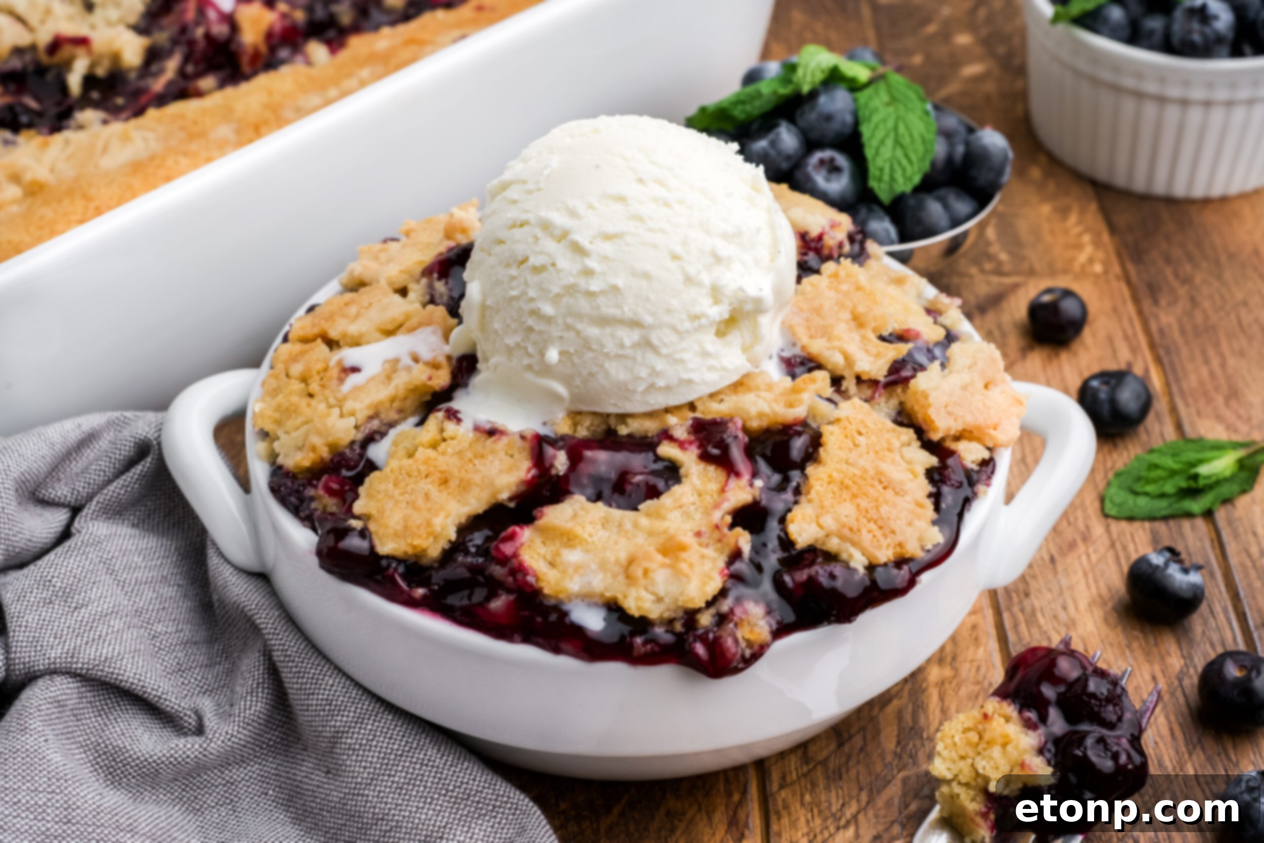 looking down on wooden table with a bowl of Blueberry Dump Cake with a scoop of ice cream in center