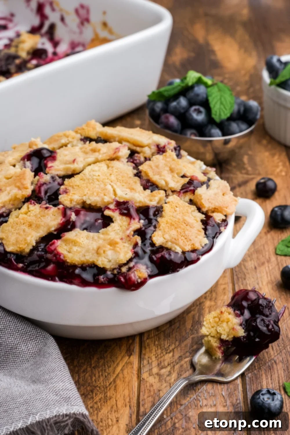 Blueberry Dump Cake in a white bowl on wooden table with blueberry and cake