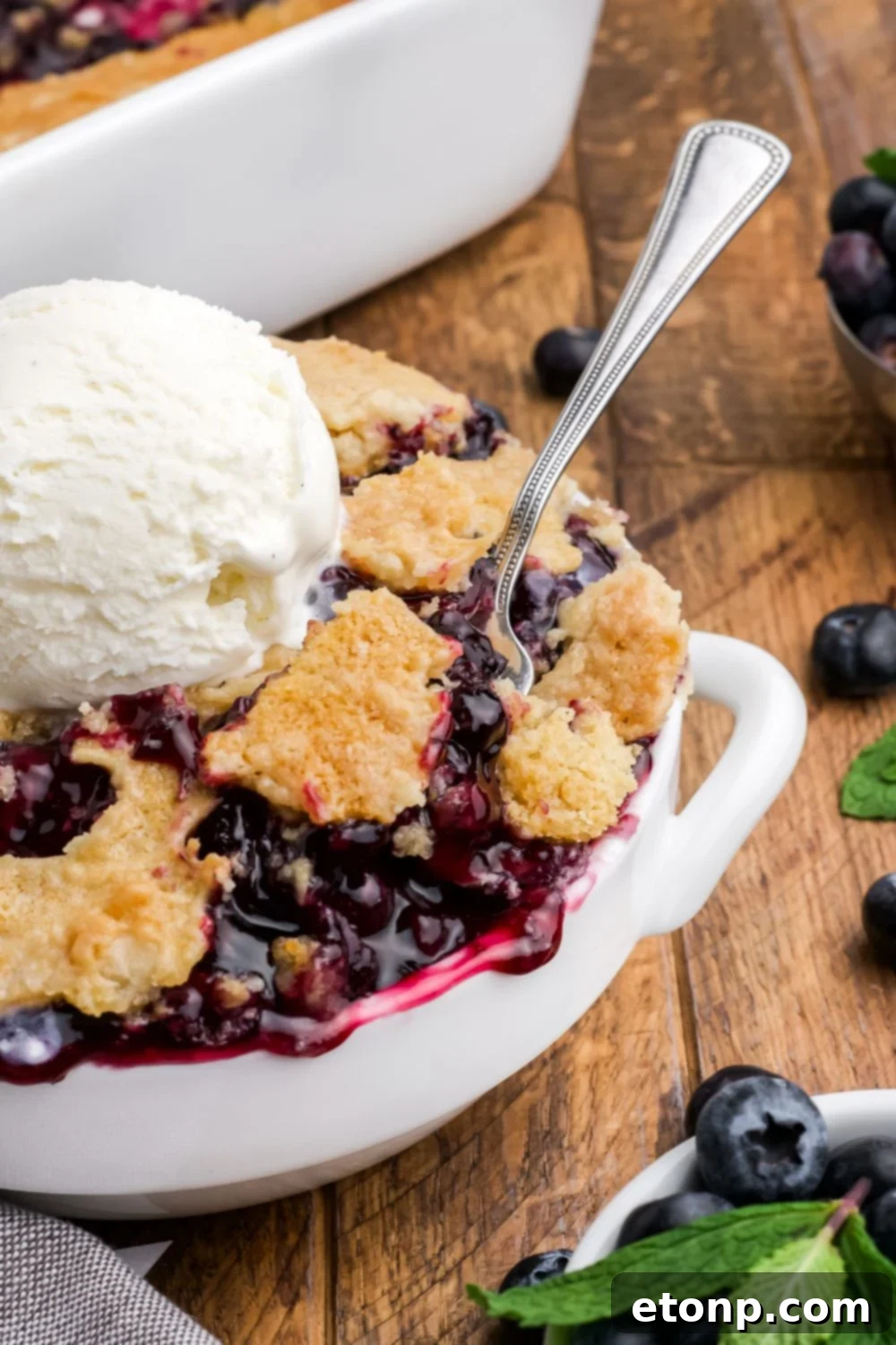 Blueberry Dump Cake in a bowl with a spoon dipping in it and a dollop of ice cream in the center of bowl