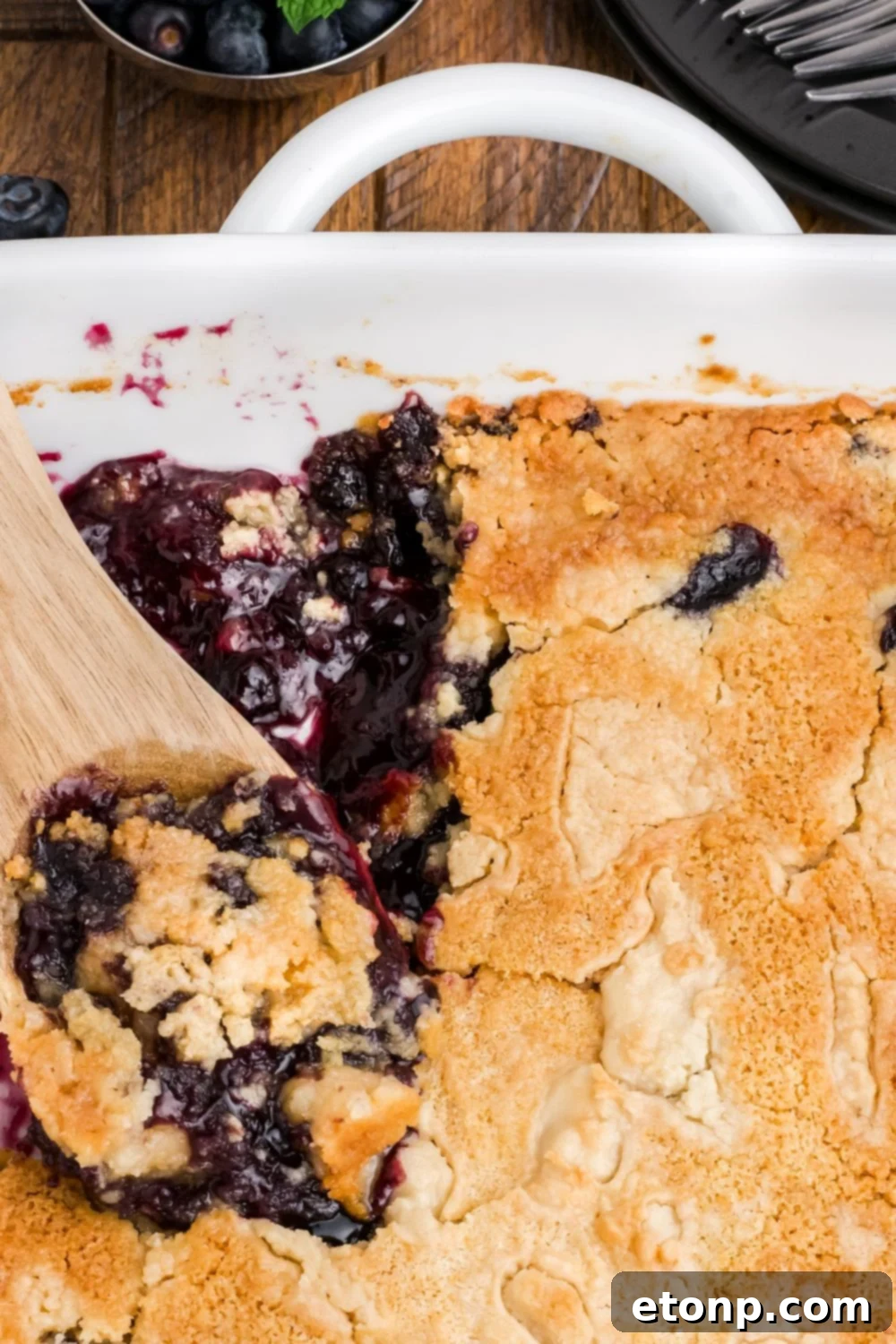 Blueberry Dump Cake in a pan with a wooden spoon scooping some up