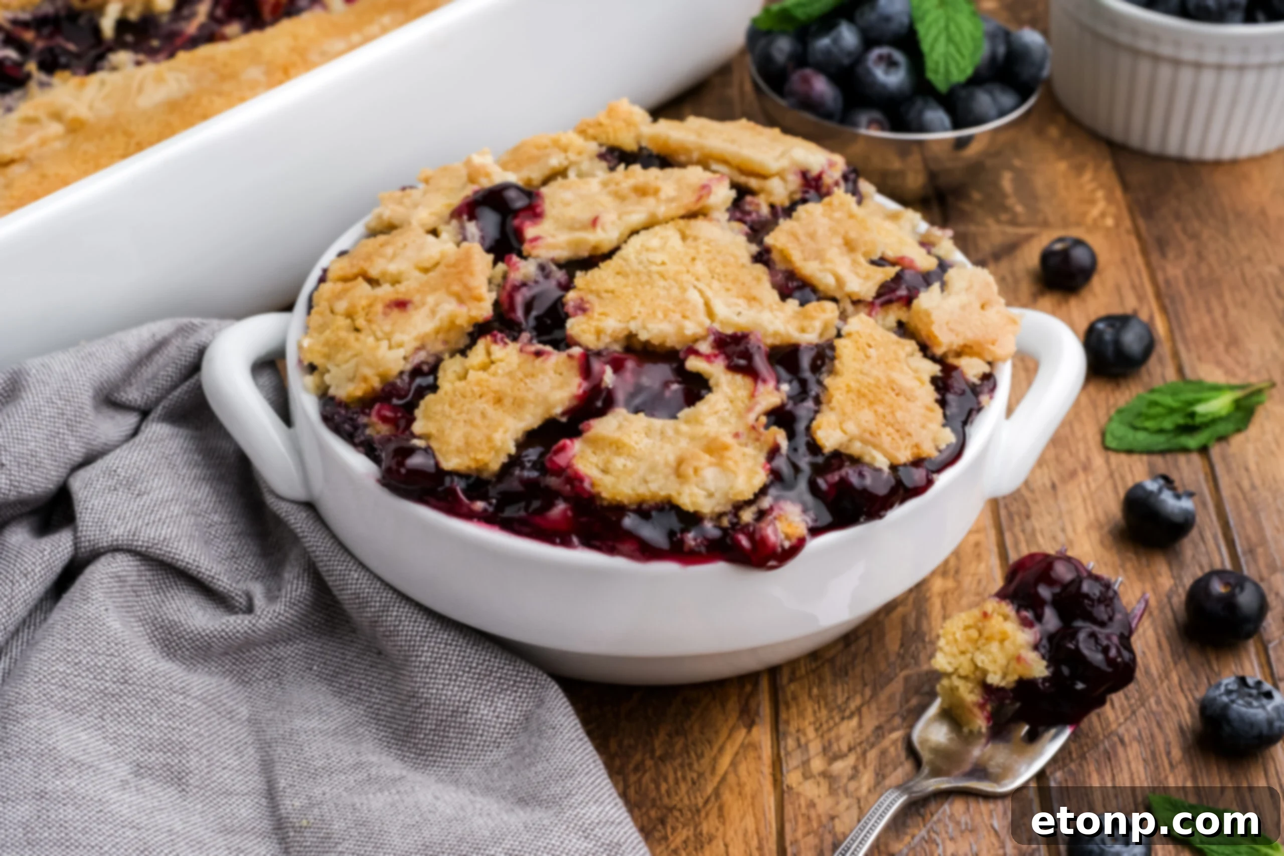 Blueberry Dump Cake in a white bowl on a dark wood table