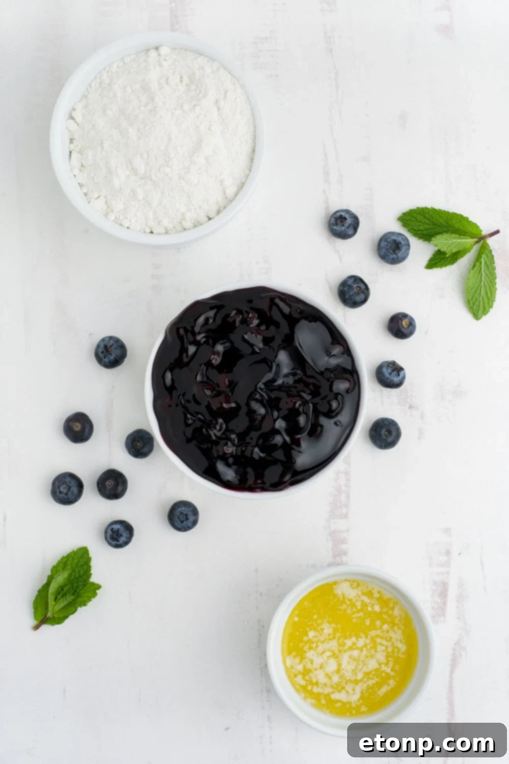 Blueberry Dump Cake ingredients in white bowls on a white table with fresh blueberries on table