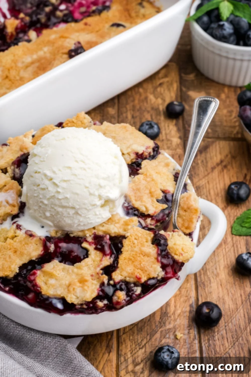 white bowl full of blueberry dump cake with a scoop of vanilla ice cream in the center