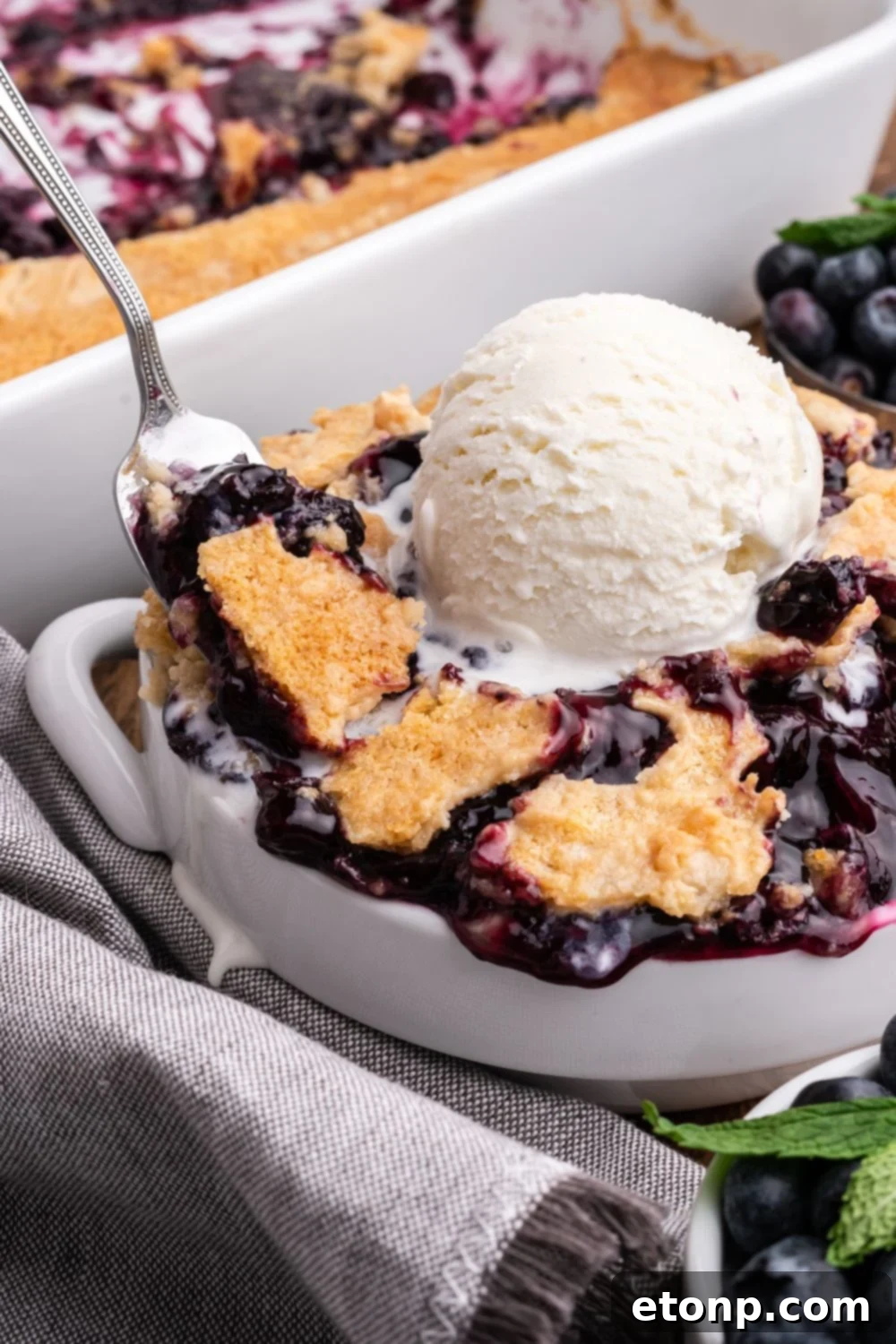 white bowl full of Blueberry Dump Cake with a spoon scooping out of the edge