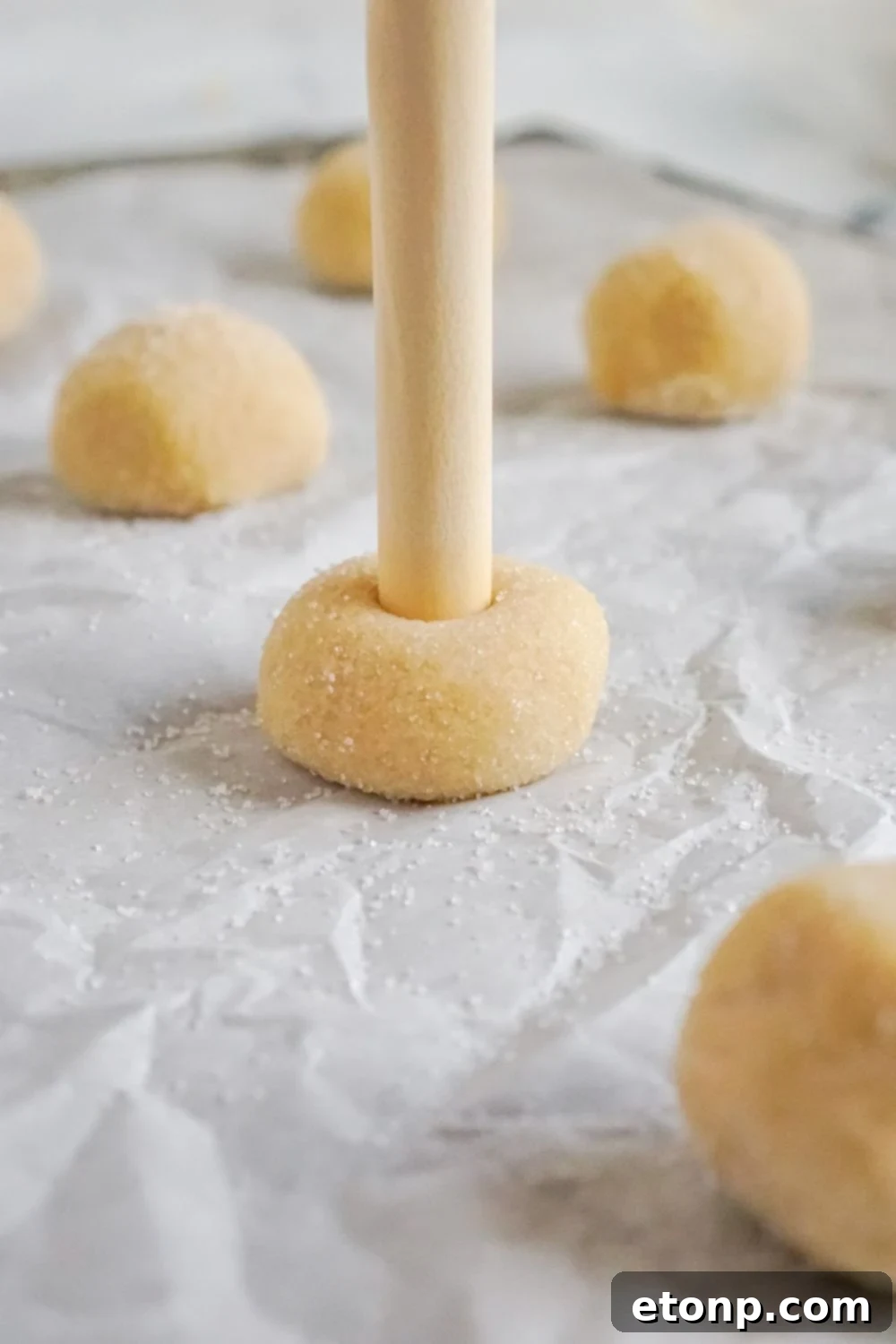 A wooden tool creating an indentation in the center of a thumbprint cookie.