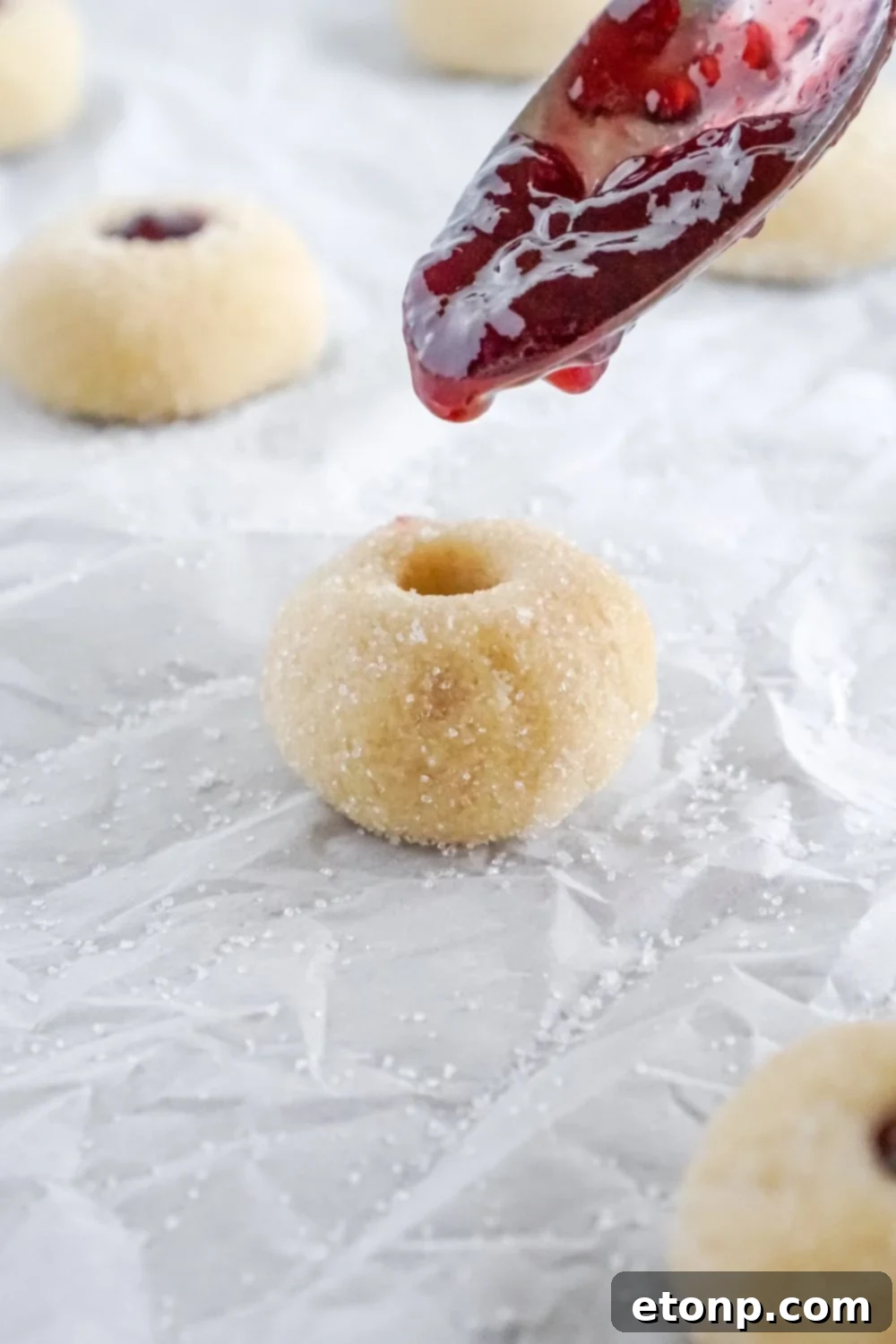 A spoon filling the center of each Raspberry Thumbprint Cookie with raspberry jam.