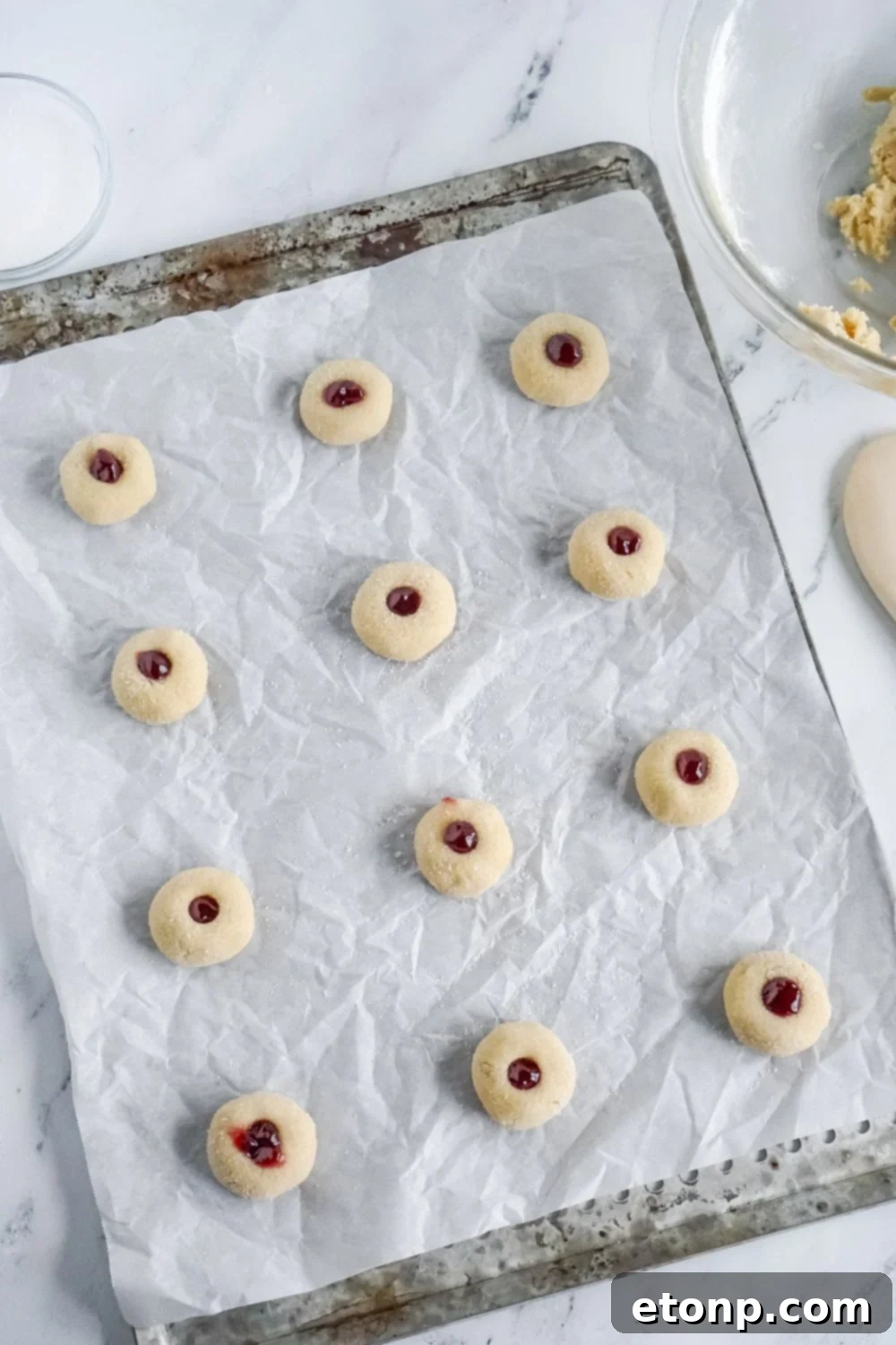 Raw Raspberry Thumbprint Cookie dough arranged on a baking sheet lined with parchment paper.