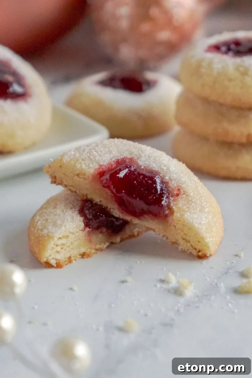 A Raspberry Thumbprint Cookie cut in half, displayed alongside a stack of cookies.