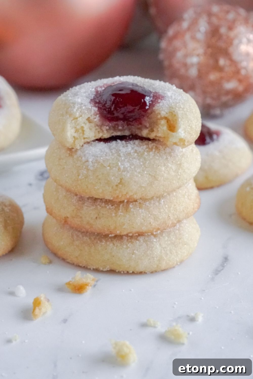 A stack of Raspberry Thumbprint Cookies with a bite taken out of the top one.
