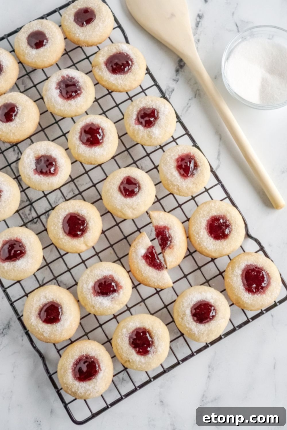 A cooling rack with Raspberry Thumbprint Cookies, one cut in half.