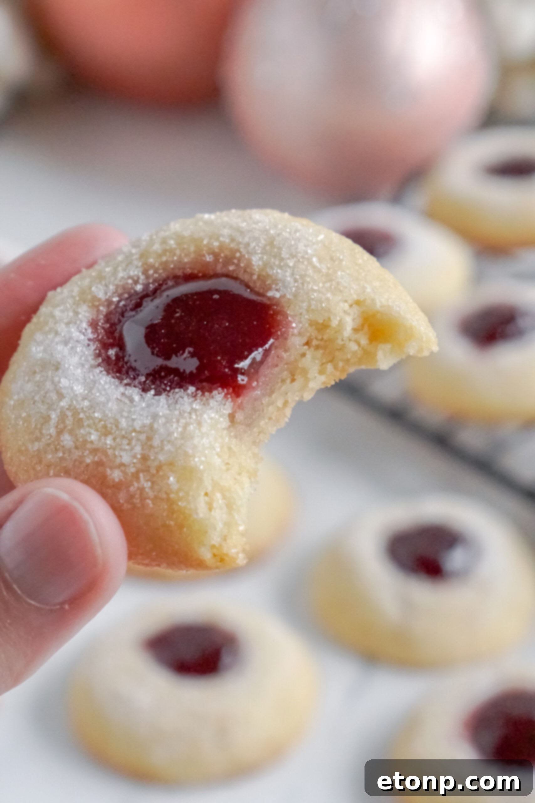 A Raspberry Thumbprint Cookie with a bite taken out, revealing its soft interior and jam filling.