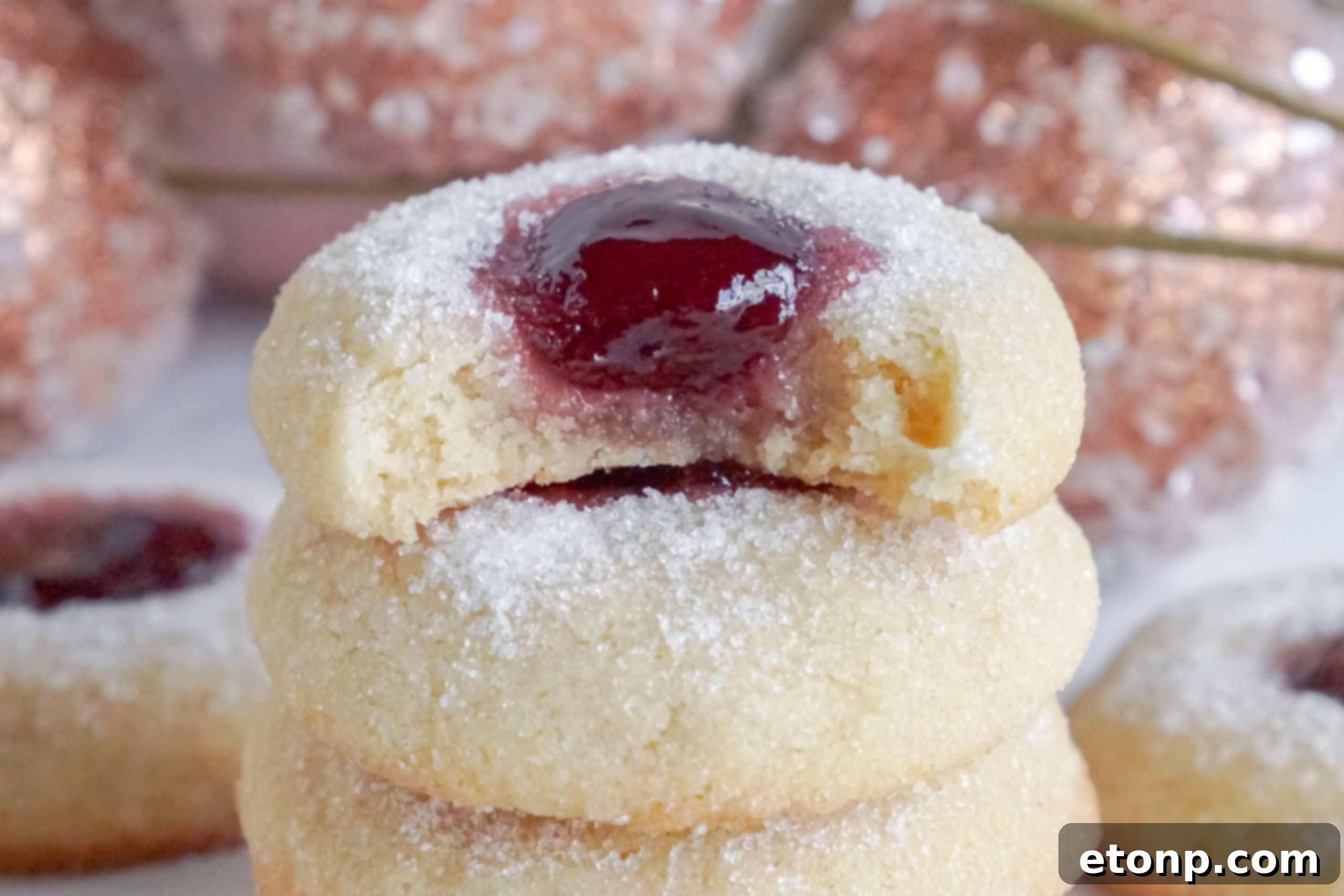 Raspberry Thumbprint Cookies stacked, with a bite missing from the top cookie.