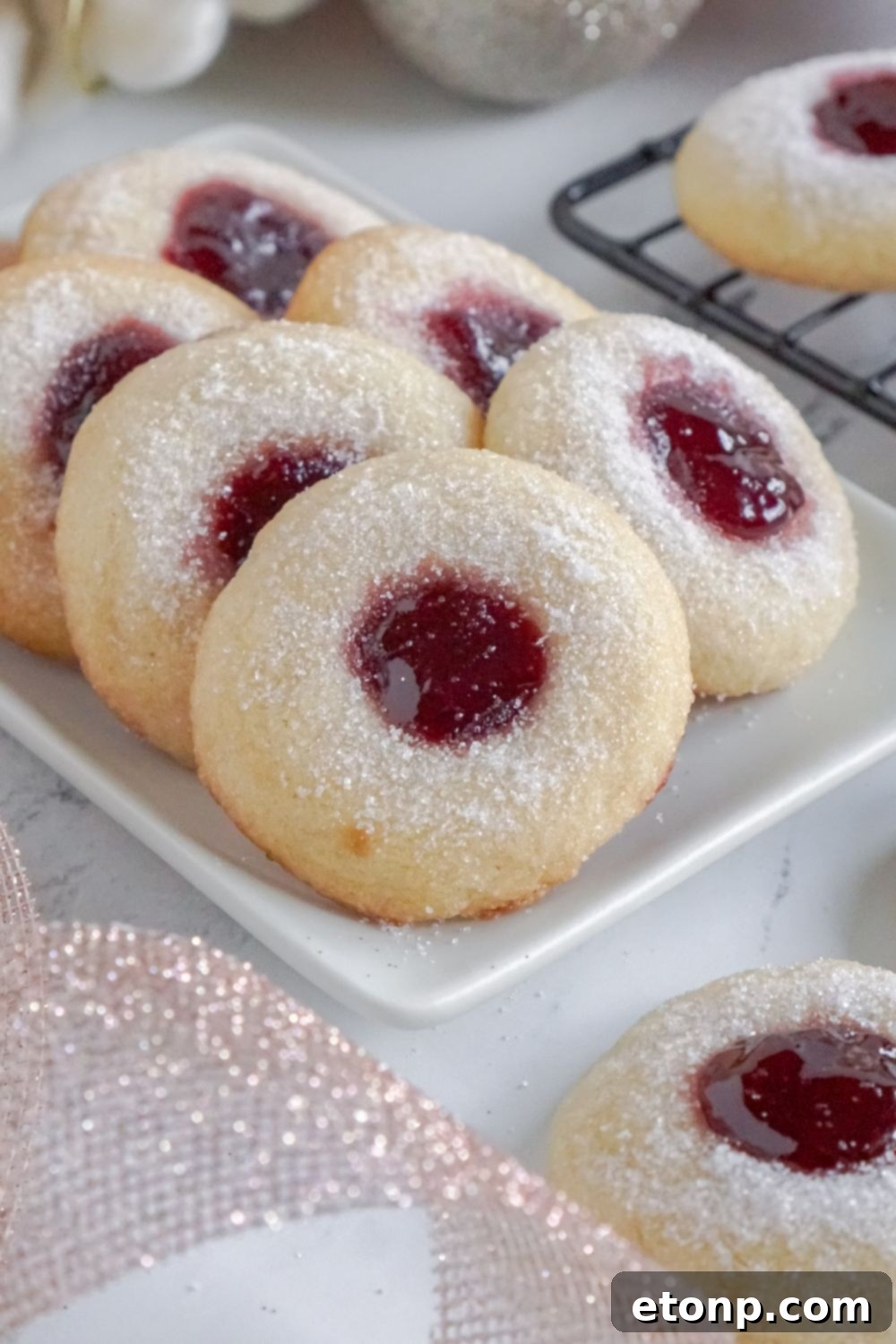 A white tray with two rows of Raspberry Thumbprint Cookies and a ribbon in front of a bowl.