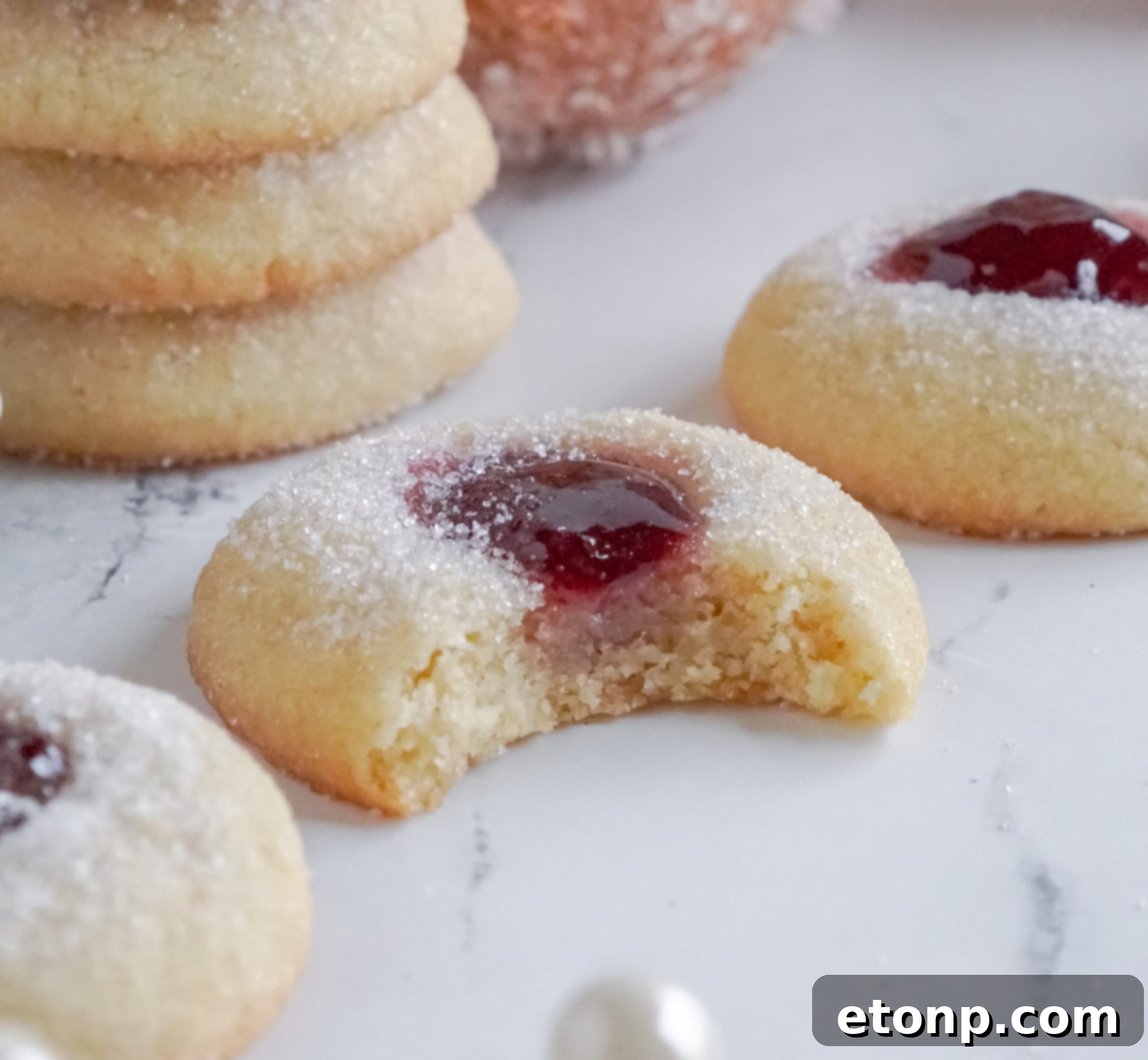 Raspberry Thumbprint Cookie with a bite missing, surrounded by other cookies on a marble table.