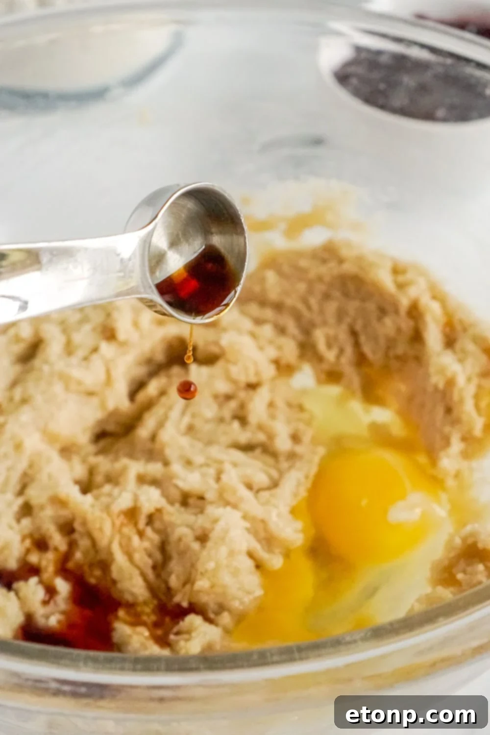 Vanilla extract being poured into a bowl of cookie dough.