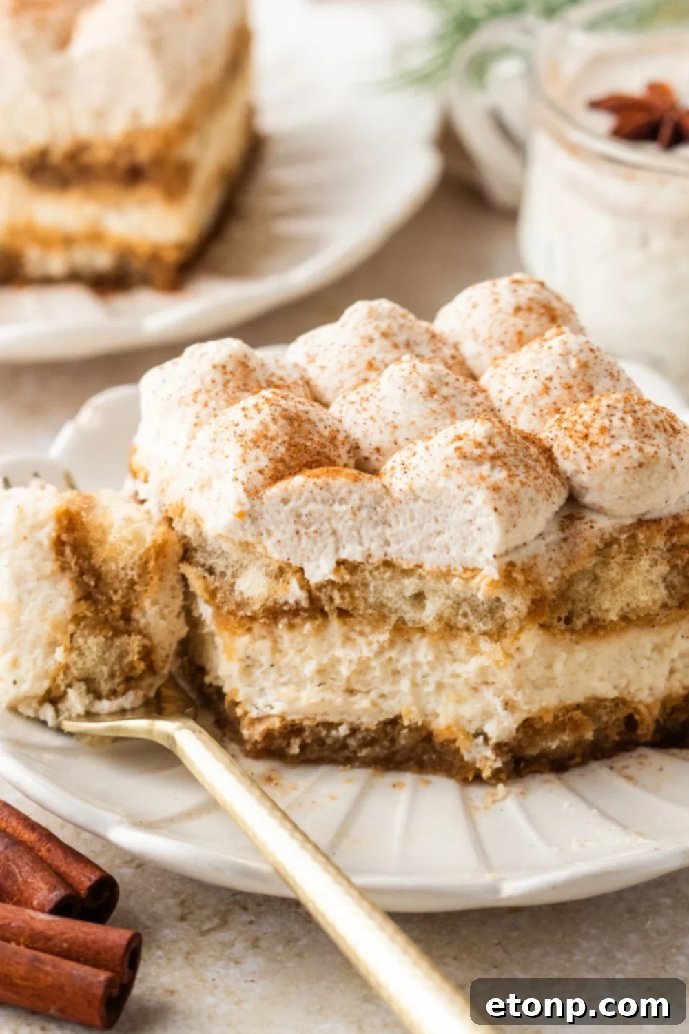 Eggnog Tiramisu: A Festive Holiday Treat 23 Eggnog Tiramisu sliced into a square on plate wit ha bite on a fork on side of plate with cinnamon sticks on table
