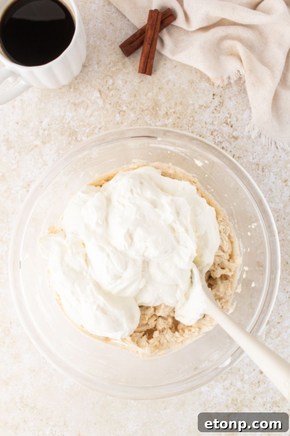Eggnog Tiramisu: A Festive Holiday Treat 8 A glass bowl on table folding in whipped cream into the eggnog tiramisu