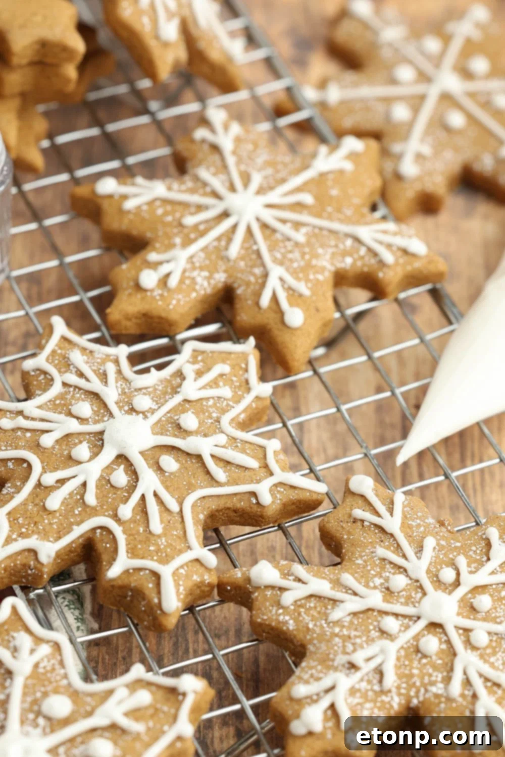 Snowflake gingerbread cookies being decorated with royal icing on a cooling rack.