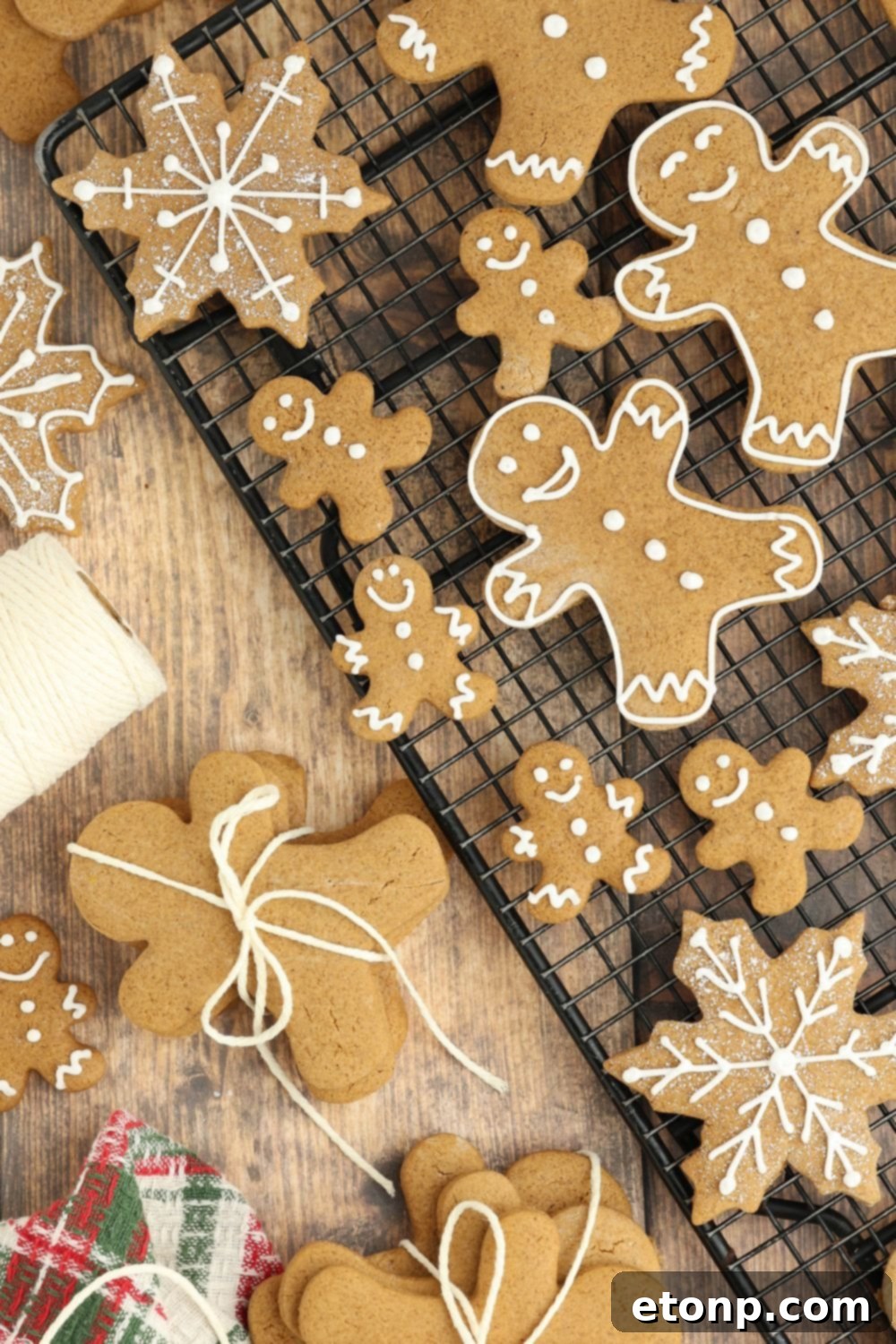 Cooling rack full of different shapes of Christmas gingerbread cookies, with string and other Christmas decorations on the table.