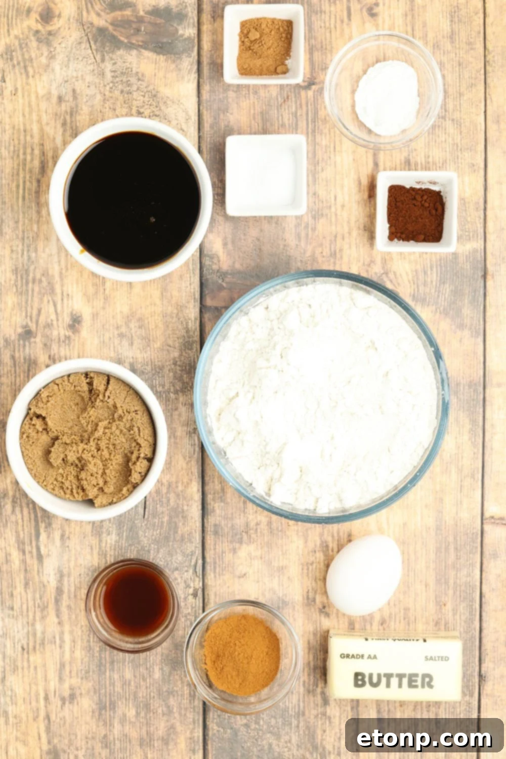 All the ingredients for Christmas gingerbread cookies arranged in single-serve bowls on a wooden table.