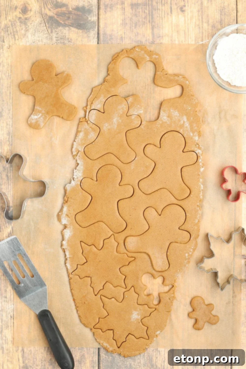 Rolled out cookie dough with gingerbread cutouts on a table.