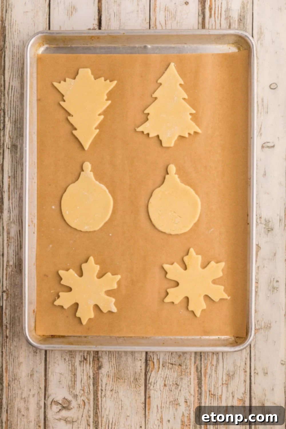 Adorned Sugar Cookies: Soft, Shapely, and Icing-Ready 12 Raw sugar cookie dough shaped like Christmas ornaments on a baking sheet.