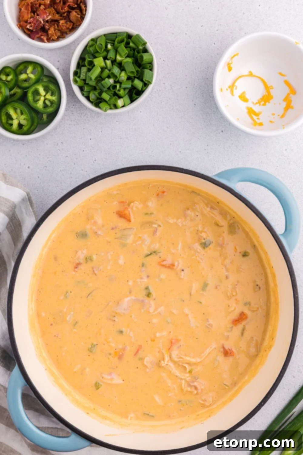 Jalapeño popper crack chicken soup in a pot with small bowls of ingredients around for toppers
