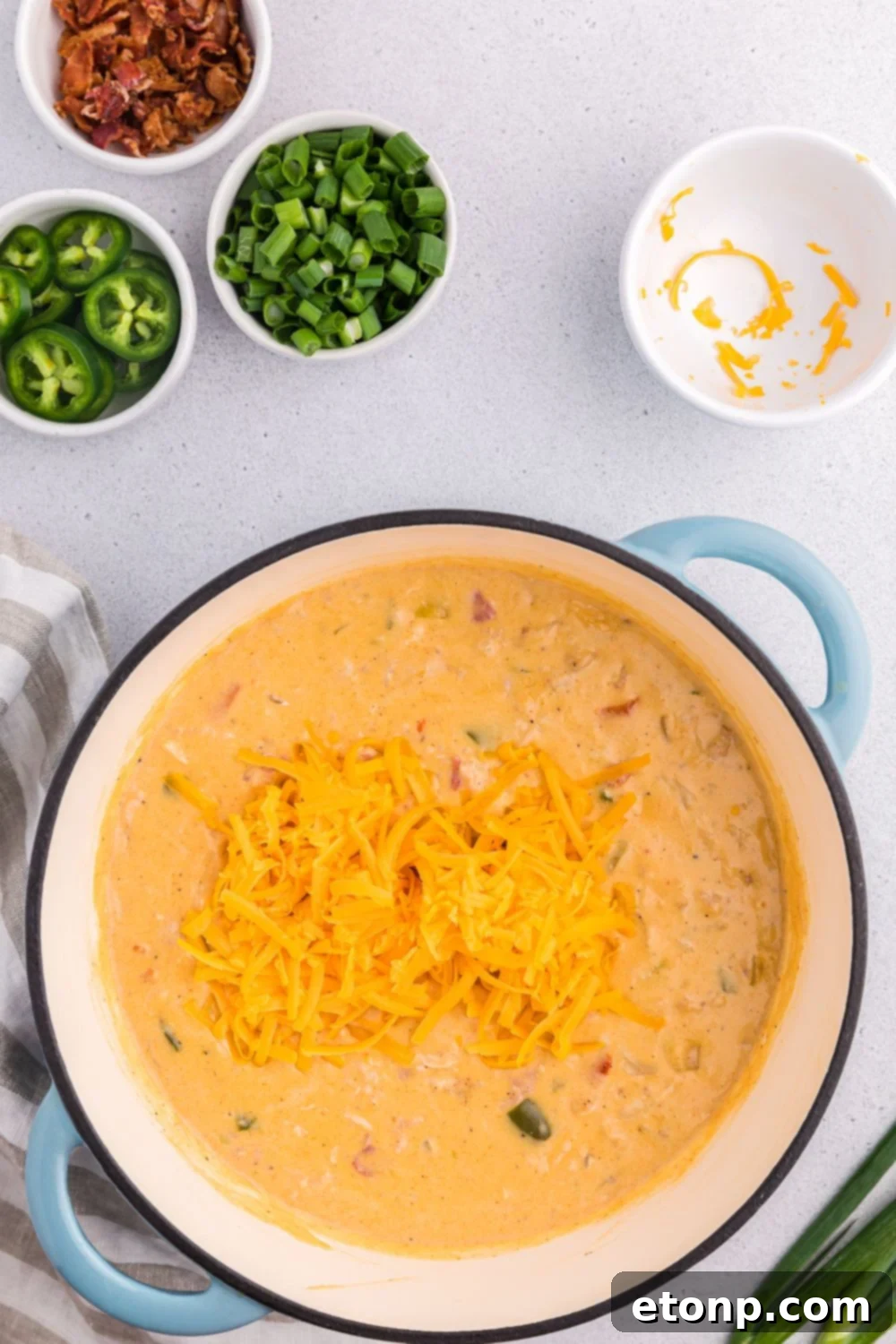 Shredded cheese poured over the top of the jalapeño popper crack chicken soup in a pot on a table