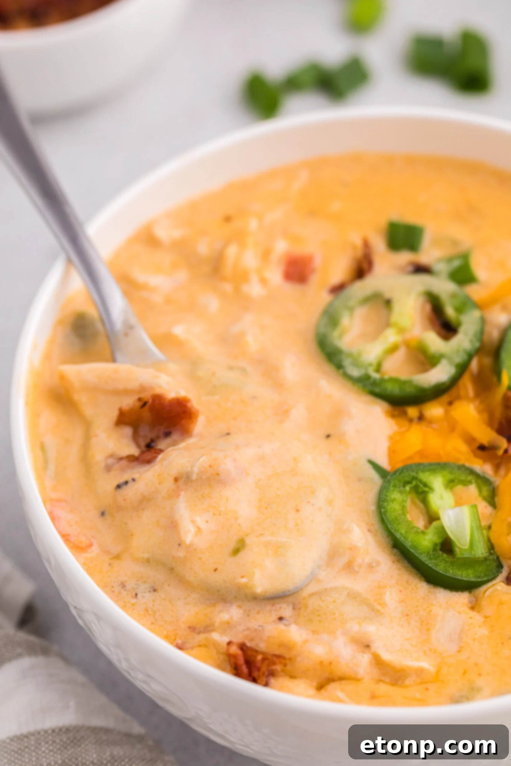 White bowl filled with jalapeño popper crack chicken soup with a spoon scooping up some of the soup