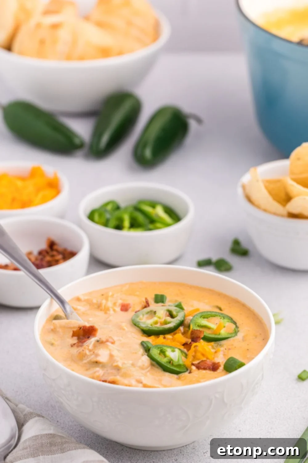 Jalapeño popper crack chicken soup in a bowl with chips, peppers, and other ingredients around the table