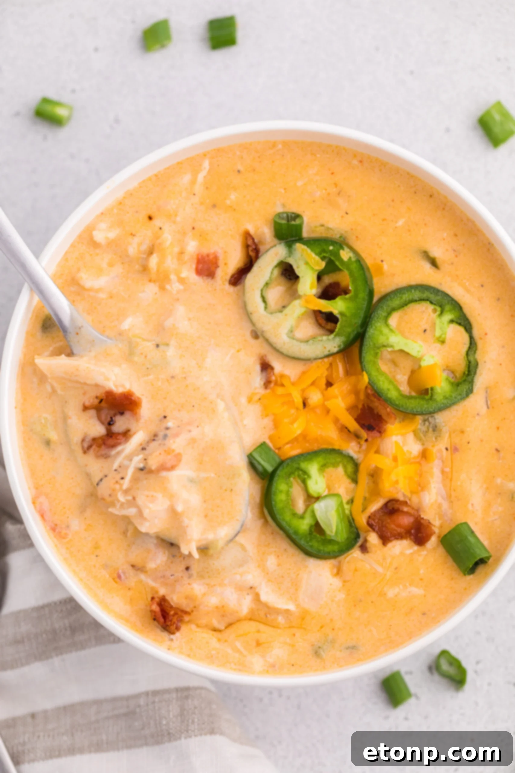 Overhead shot of a white bowl filled with jalapeño popper crack chicken soup with a spoon scooping up some of the soup