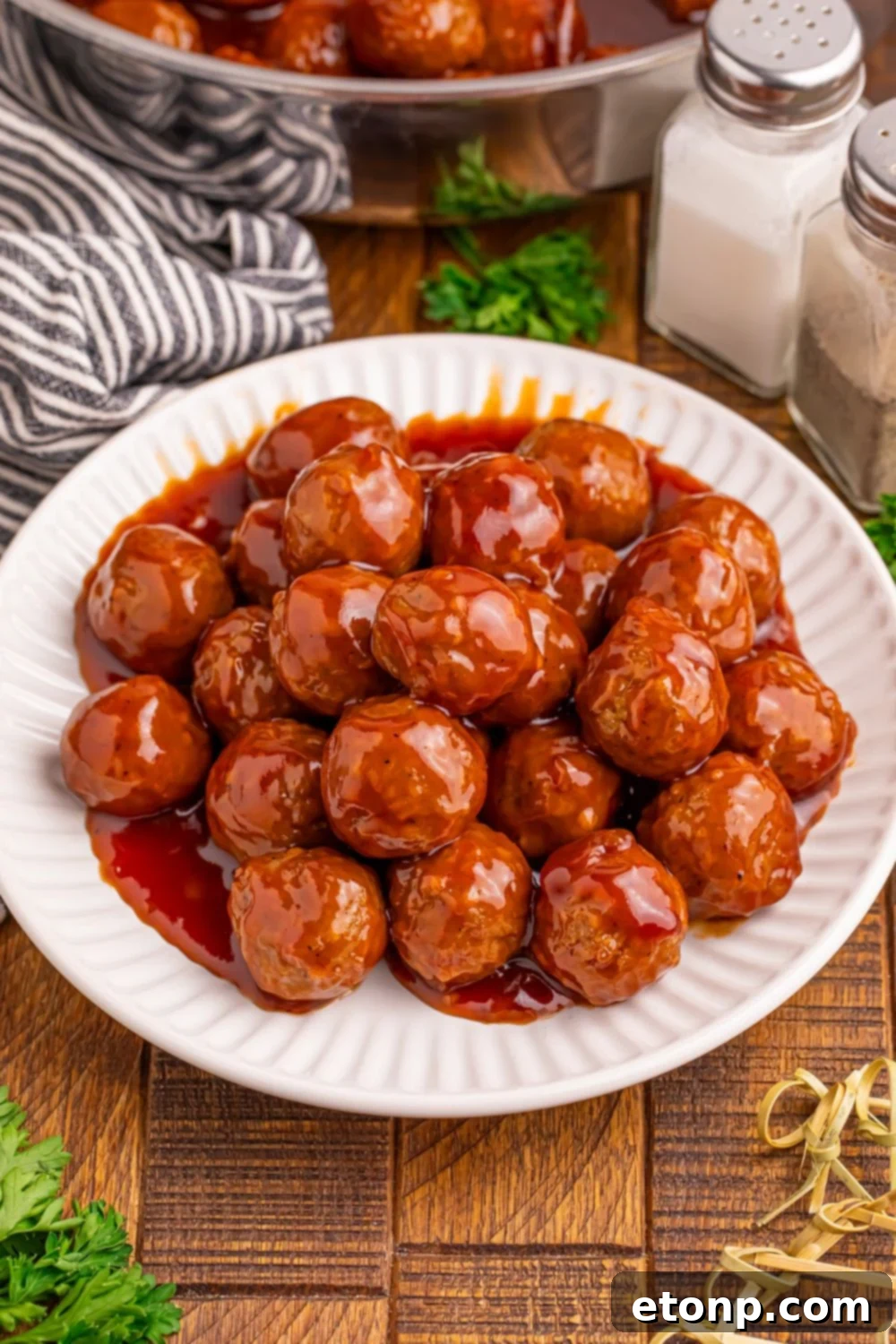 Peach BBQ Meatballs on a white plate, surrounded by toothpicks and a skillet.