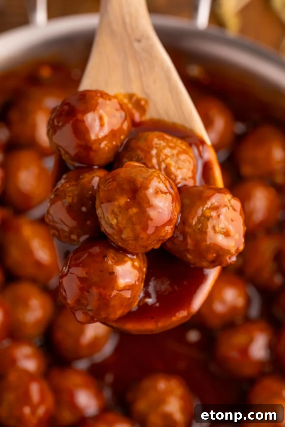 Peach BBQ Meatballs on a wooden spoon above a skillet.