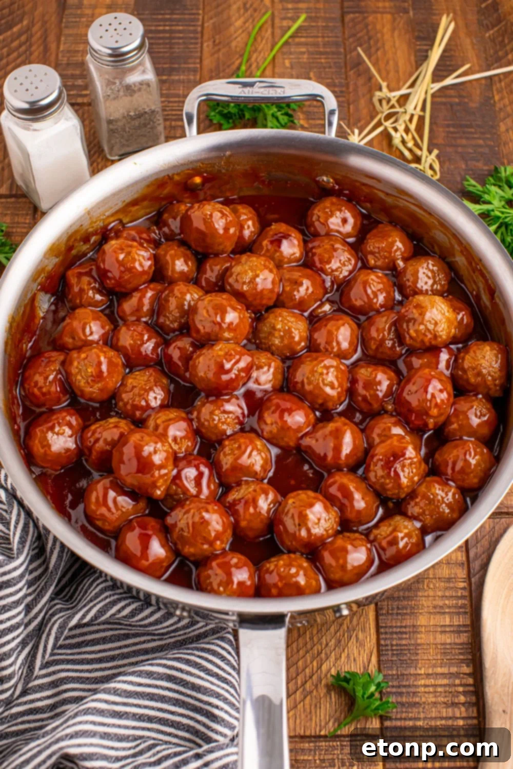 Peach BBQ Meatballs simmering in a skillet with a blue towel nearby.