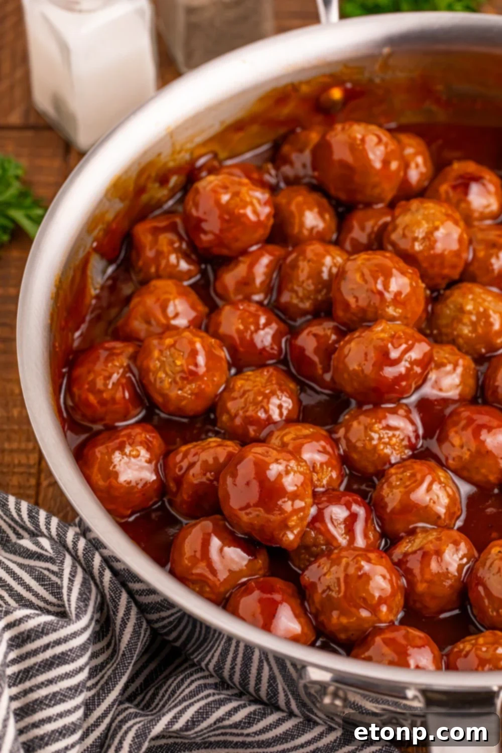 Peach BBQ Meatballs in a skillet on a table with a dish towel beside the pan.