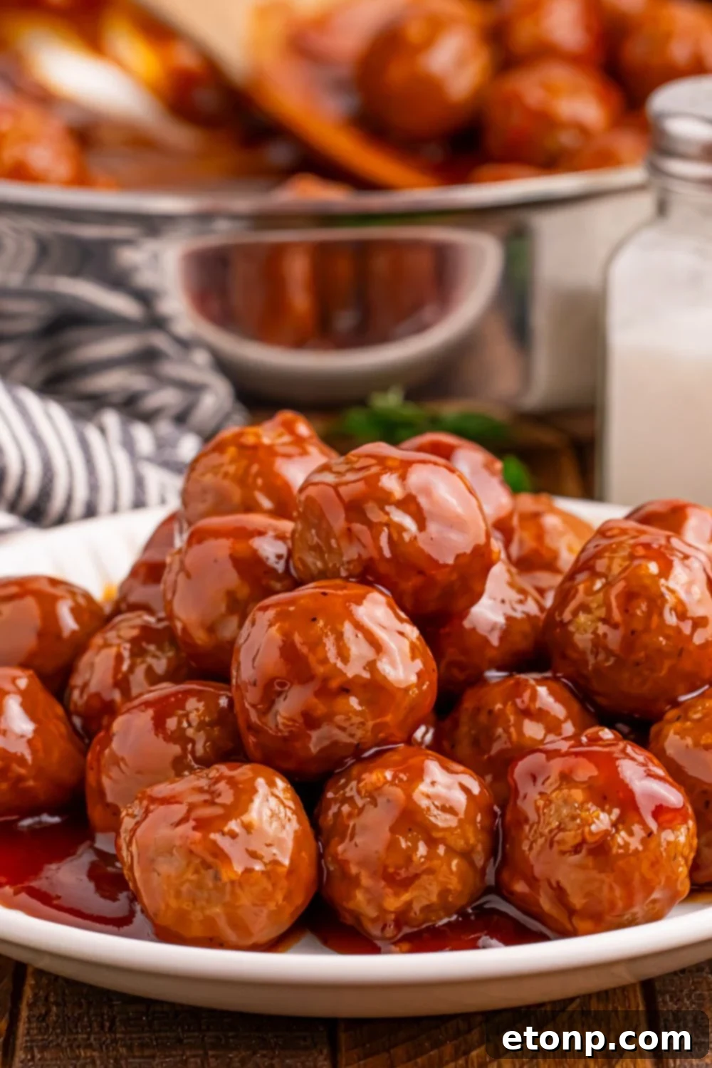 Peach BBQ Meatballs on a white plate, with a skillet in the background.