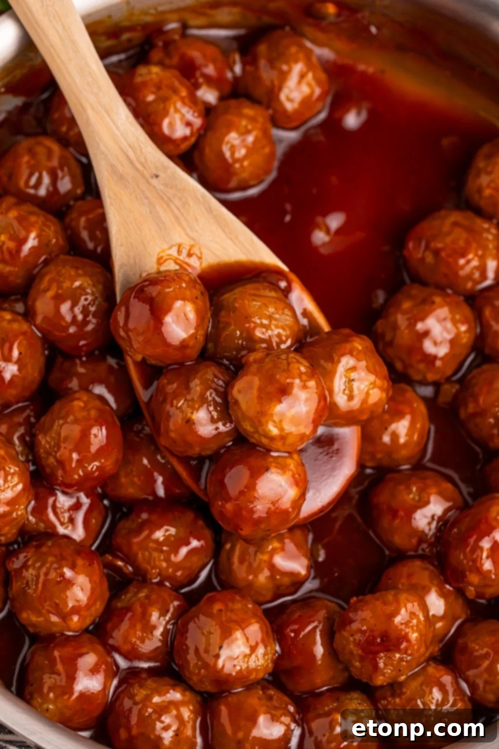 Peach BBQ Meatballs in a skillet being scooped with a wooden spoon.