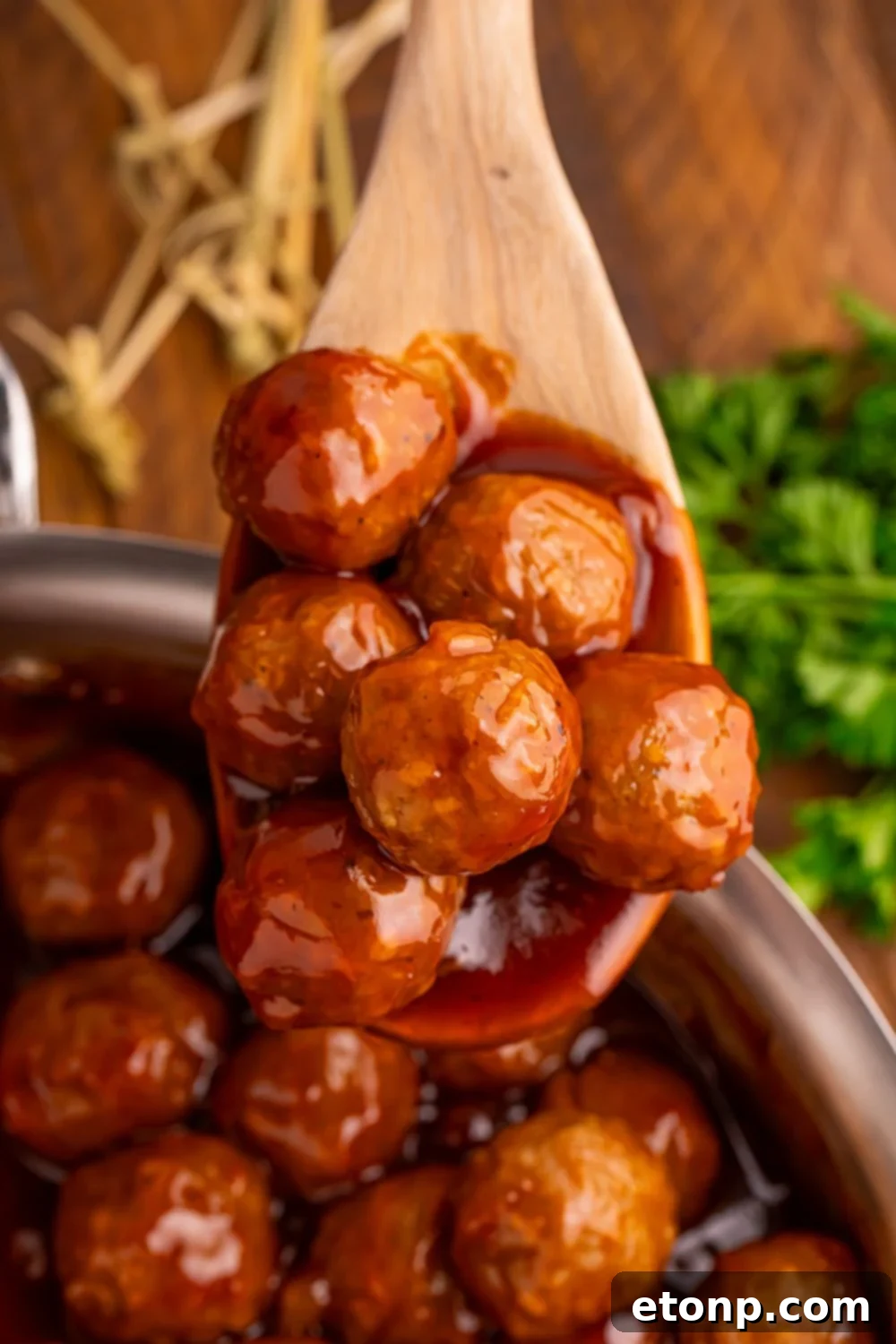 Peach BBQ Meatballs in a skillet with a wooden spoon and fresh parsley, ready to be served.