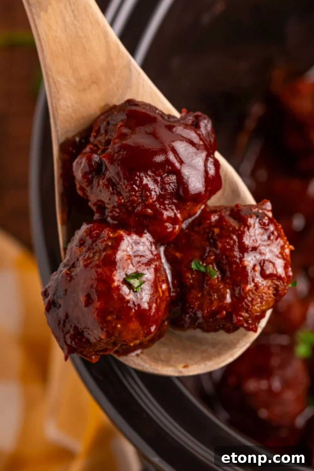 Slow-Cooker BBQ Meatball Magic 23 Crockpot Homemade BBQ Meatballs being lifted out of the crockpot with a wooden spoon