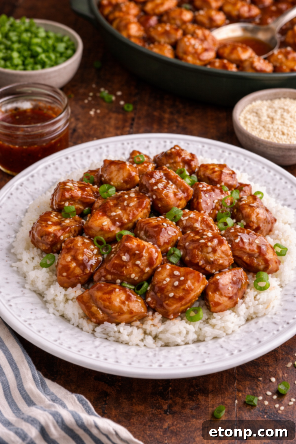 Bourbon Chicken piled on top of a plate with rice, sesame seeds, and green onions