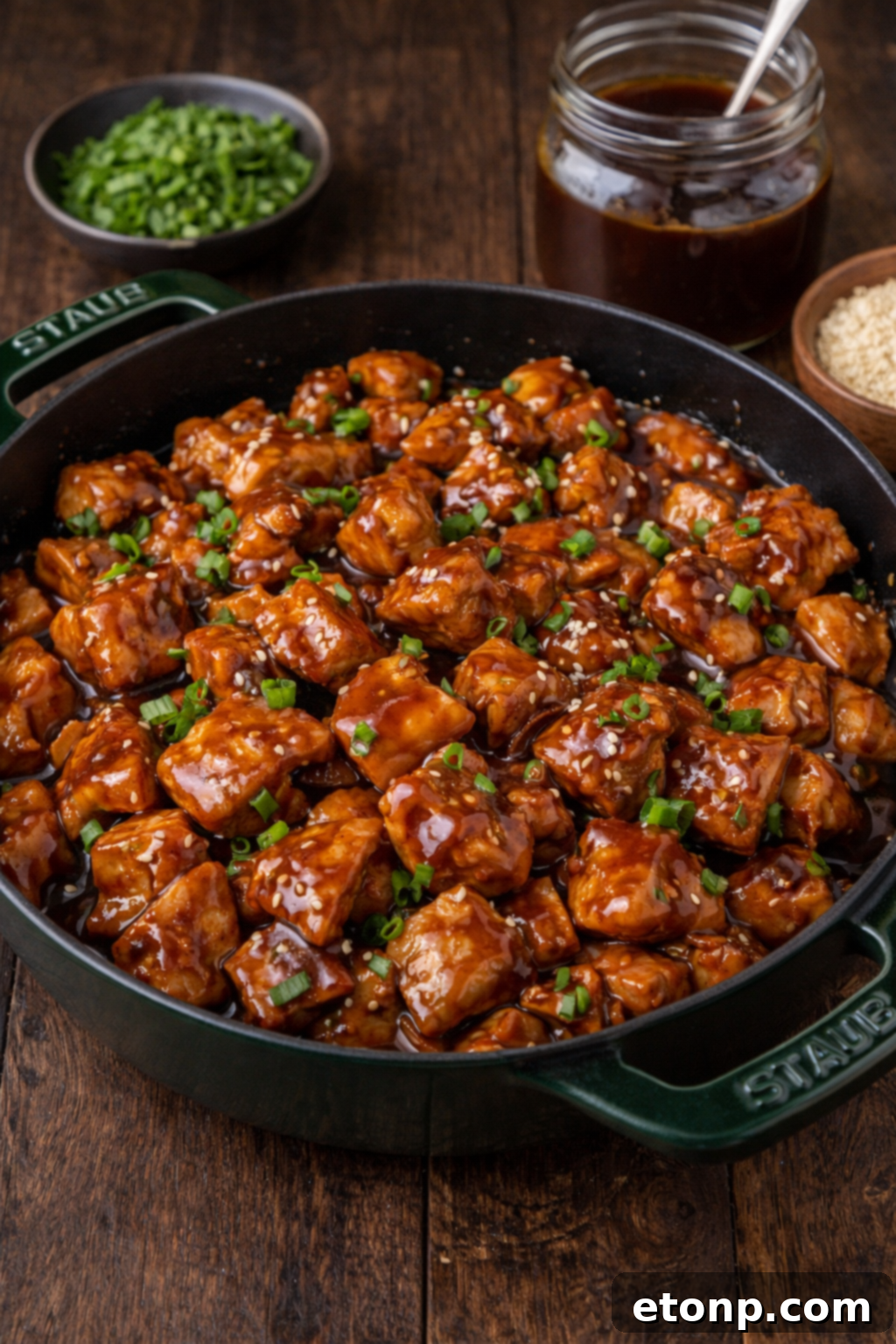Bourbon Chicken in a green skillet with sesame seeds and chives