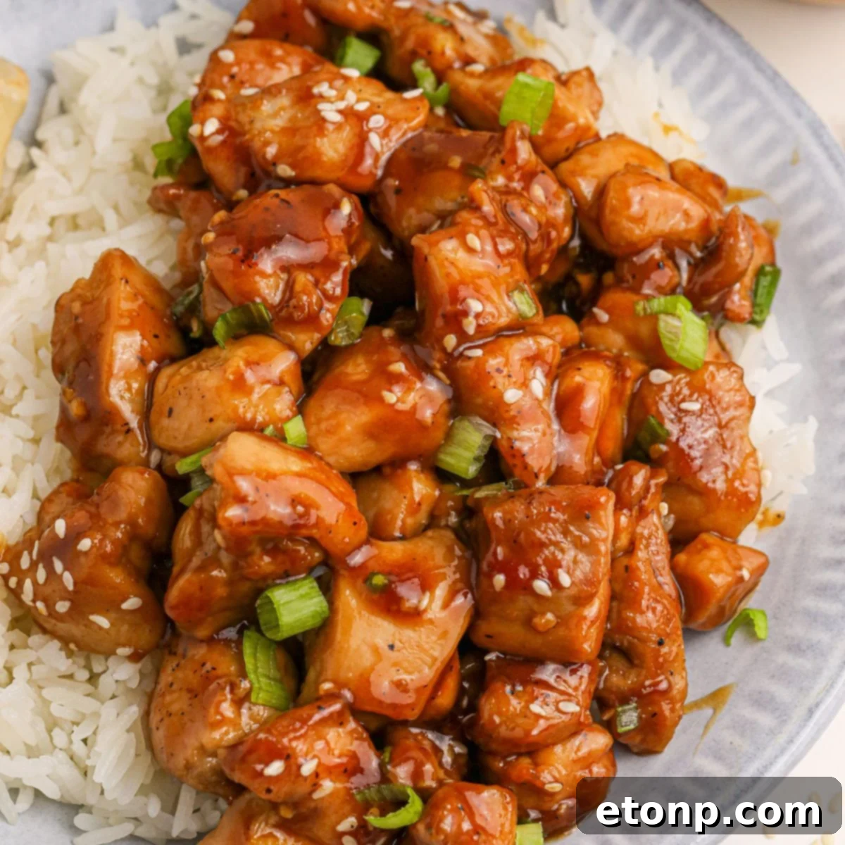 Bourbon Chicken served on a plate with rice, sesame seeds, and green onions