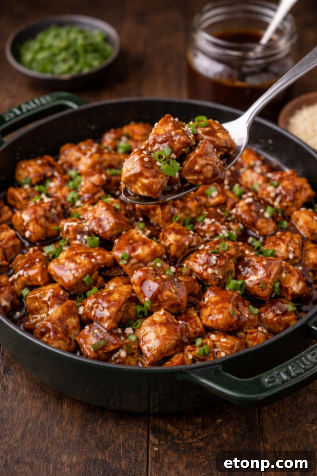 Bourbon Chicken in a skillet with a spoon lifting a bite