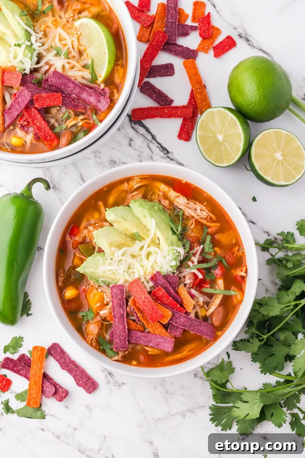 Southwestern Chicken Soup in bowls on a marble table with cilantro, peppers, and sliced limes on the table 