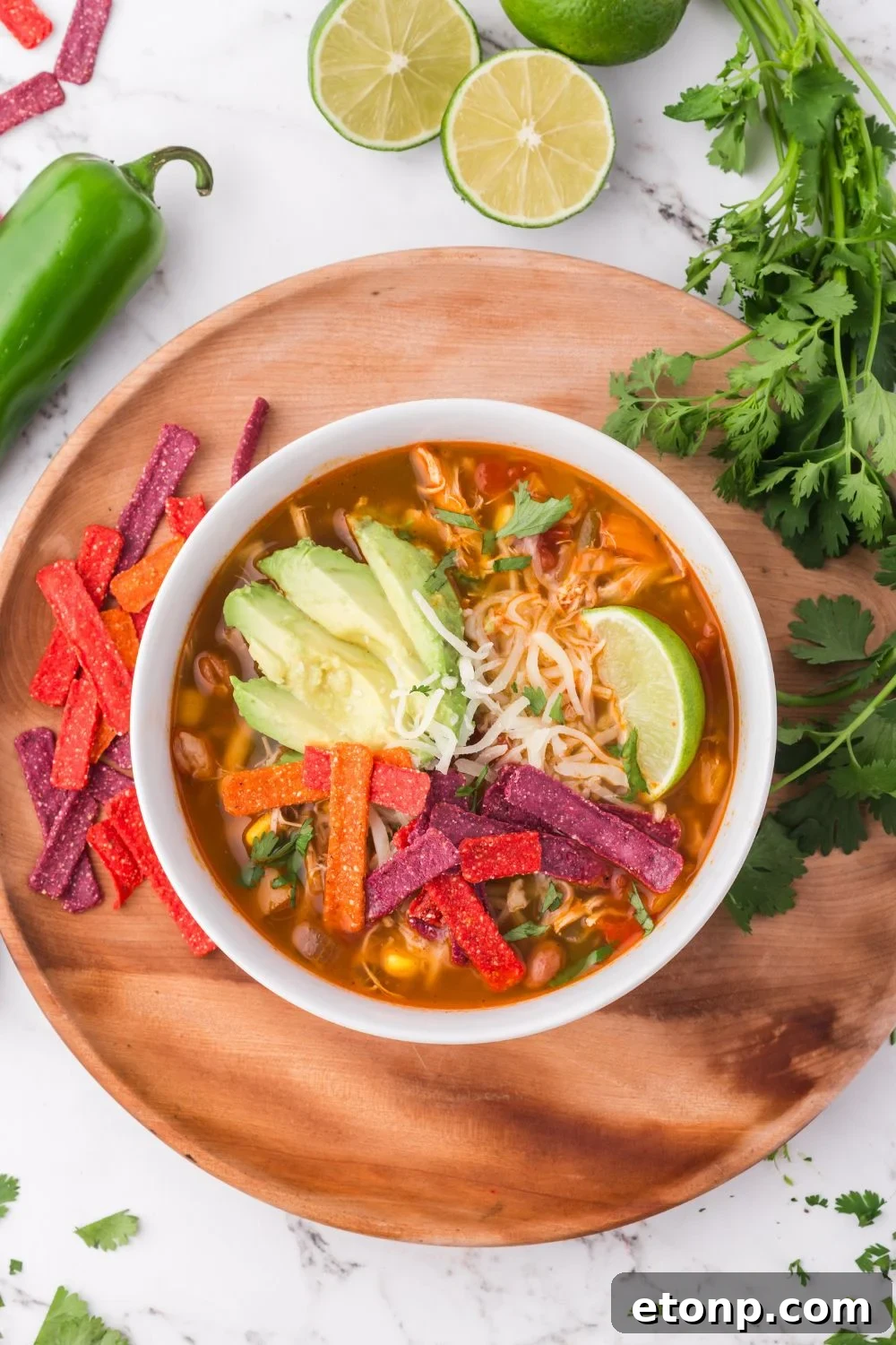 Southwestern Chicken Soup in a white bowl sitting on a round wooden board, with all the topping ideas spread around on the table 