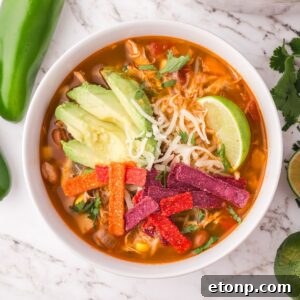 Southwestern Chicken Soup in a white bowl topped with tortilla chips, avocado, lime wedge, and more