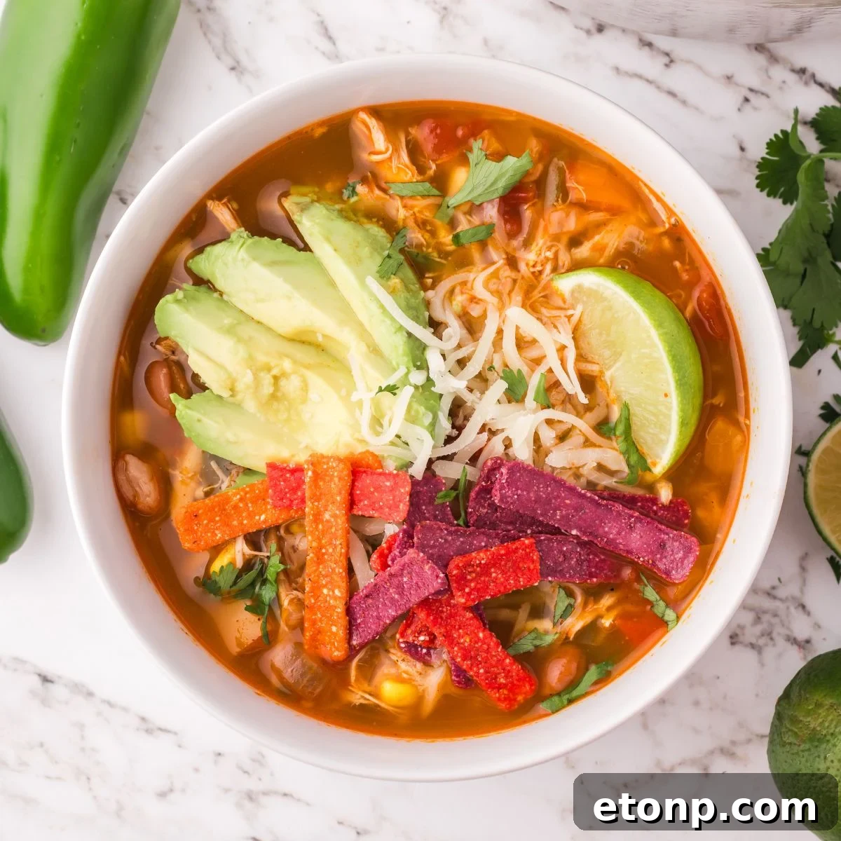 Southwestern Chicken Soup in a white bowl topped with tortilla chips, avocado, lime wedge, and more 
